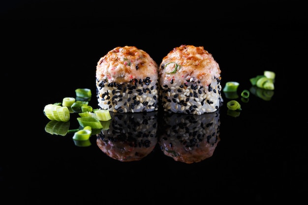 Apetitoso rollo de sushi al horno con pescado, cebolla verde sobre un fondo negro con reflejo Menú y restaurante