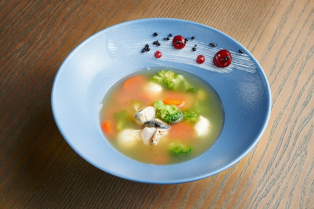 Foto apetitoso y saludable caldo de mariscos con brócoli, zanahorias, mozzarella y ostras en un recipiente de cerámica azul sobre una superficie de madera. efecto de película durante la publicación. enfoque suave