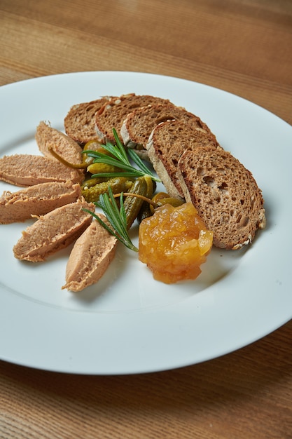 Apetitosos antipasti - pasta de ganso con mermelada, romero y pan de centeno en plato blanco sobre mesa de madera /