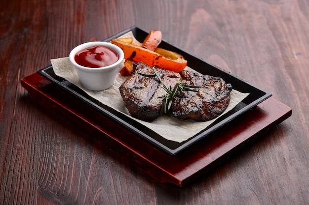 Apetitosos platos de carne a la parrilla con salsa en una mesa de madera oscura.