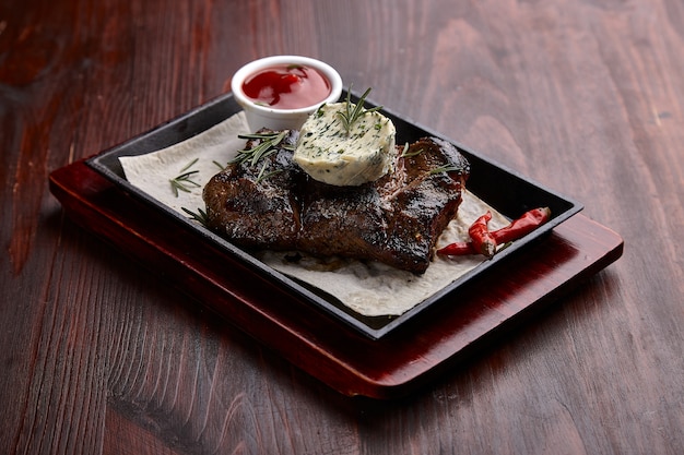 Apetitosos platos de carne a la parrilla con salsa en una mesa de madera oscura.