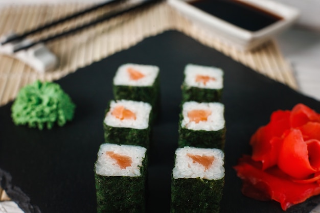 Apetitosos y sabrosos rollos de sushi con delicioso salmón servido en pizarra negra con jengibre y wasabi. Mariscos japoneses.