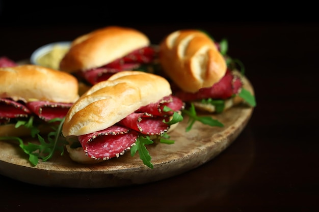 Apetitosos sanduíches de salame com rúcula e mostarda em uma placa de madeira