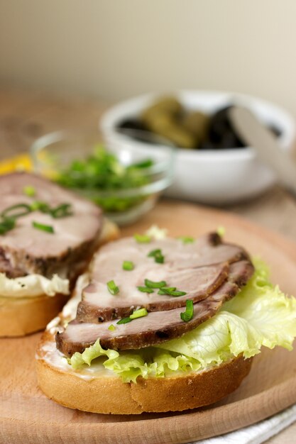 Apetitosos sándwiches con carne, lechuga y salsa servidos con aceitunas. Estilo rústico