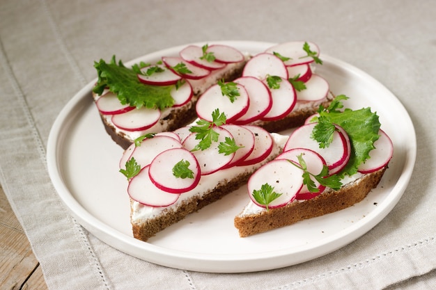 Apetitosos sándwiches de pan de centeno con requesón, rábanos y lechuga. Estilo rústico