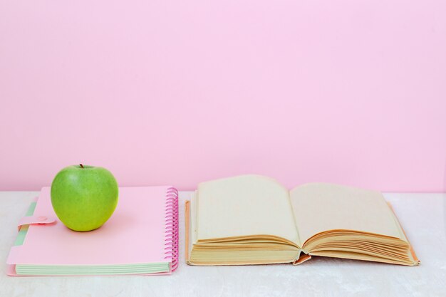 Apfel, Buch, Heft auf dem Schreibtisch auf rosa Hintergrund