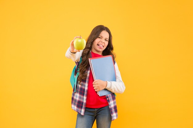 Apfel ist jetzt außerhalb der Saison Kleines Kind machen Gesicht hält Apfel und Bücher gelben Hintergrund Saurer Apfel Vitamin Schulsnack Gesunde Ernährung und Ernährung Organische und natürliche Ernährung Gesundheitserziehung