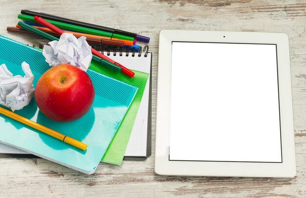 Apfel mit Schulmaterial und Tablette mit leerem Bildschirm auf weißem Holztisch