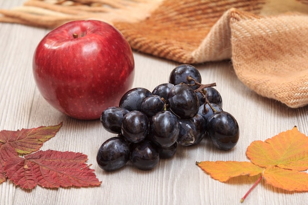 Apfel, Trauben, kariertes Plaid und trockene Blätter auf Holzbrettern. Ein Herbststillleben.