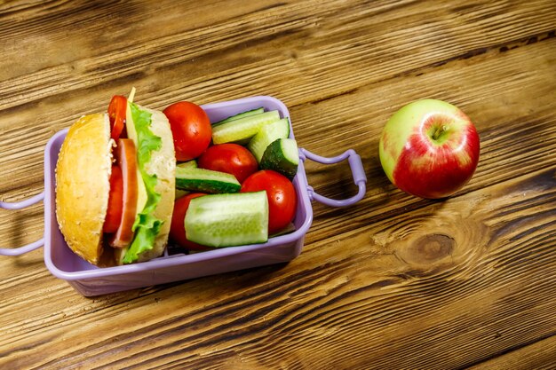 Apfel- und Brotdose mit Burgern und frischem Gemüse auf einem Holztisch