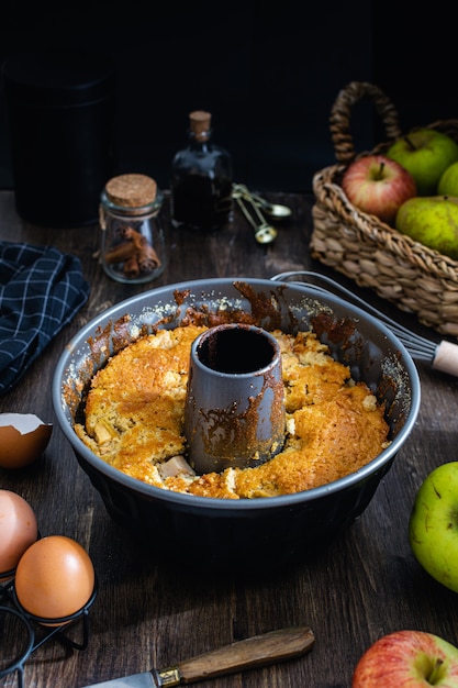 Apfelbundt-Kuchen auf dunklem Holztisch, Eiern, Zimt, Vanilleextrakt