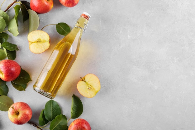Apfelessig in einer Glasflasche und frische Äpfel mit Blättern auf hellem Hintergrund Draufsicht flach liegen