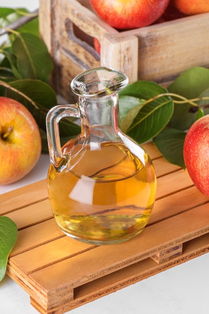 Apfelessig in einer Glasflasche und frische Äpfel mit Blättern auf hellem Hintergrund