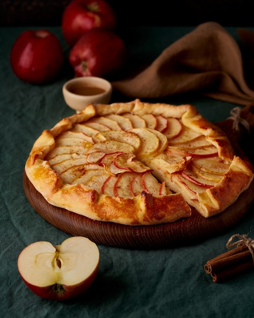 Apfelkuchen, Galette mit Früchten, süßes Gebäck auf dunkelgrüner Tischdecke, vertikal