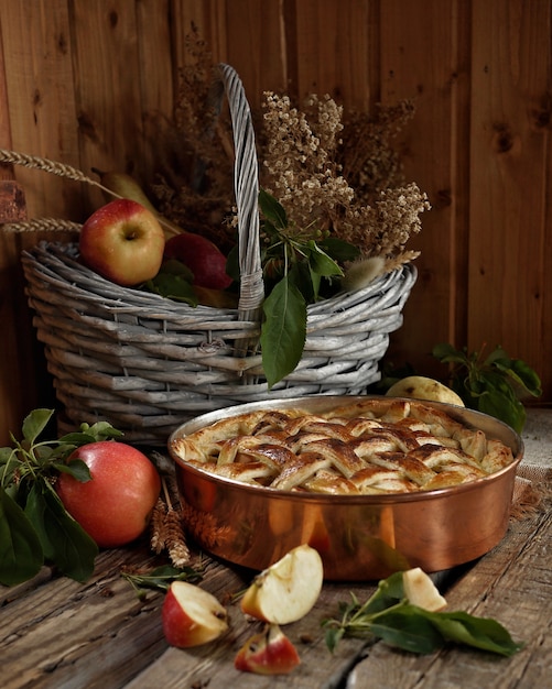 Apfelkuchen in Kupferform. Äpfel und Feldblumen im alten Korb. Rustikaler Stil