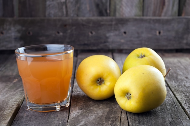 Apfelsaft in Glas und Äpfeln auf dem alten hölzernen Hintergrund