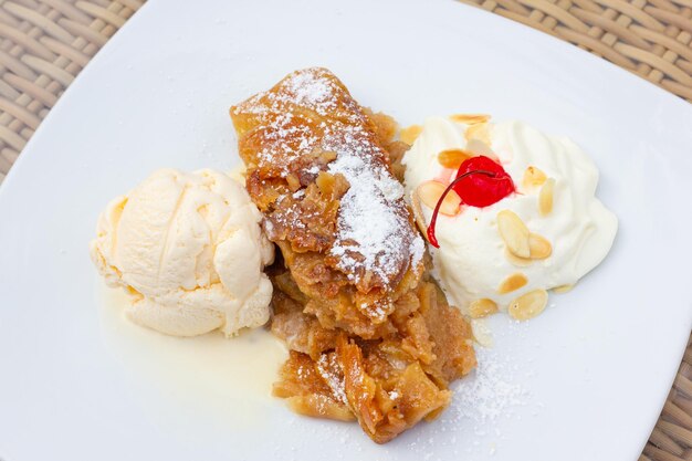 Apfelstrudelkuchen auf Puderzucker, Vanilleeiskugel und Schlagsahne mit Mandeln