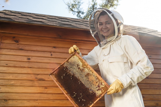 Apicultor feminino jovem segurar a moldura de madeira com favo de mel.