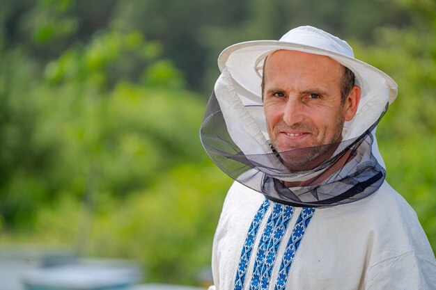 Apicultor macho sobre fondo de colmenas. Sombrero protector. Fondo borroso. Miel y abejas.