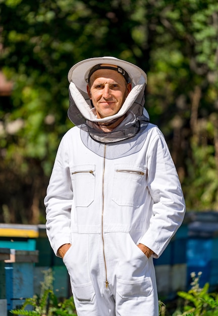 Apicultor masculino em roupa de trabalho protetora. fundo de urticária no apiário. homem nos apiários na primavera.