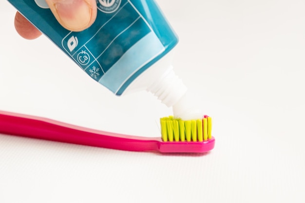 Aplastando la pasta de dientes en un cepillo de dientes sobre un fondo blanco