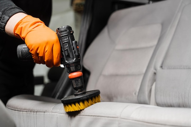 Aplicação de detergente em assento têxtil no interior do carro para limpeza a seco Espalhar detergente em assentos têxteis de carro usando broca com escova para limpeza a seco