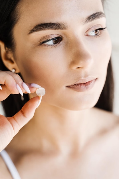 Aplicação de remendo redondo de acne na bochecha de uma menina jovem usando adesivos de acne para tratamento de espinhas e rosácea Cosmetologia de limpeza de rejuvenescimento facial
