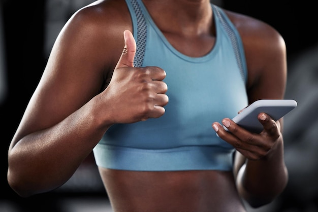 Esta aplicación me ayudó a alcanzar mi peso ideal Fotografía de una joven deportista que muestra el pulgar hacia arriba mientras usa su teléfono celular