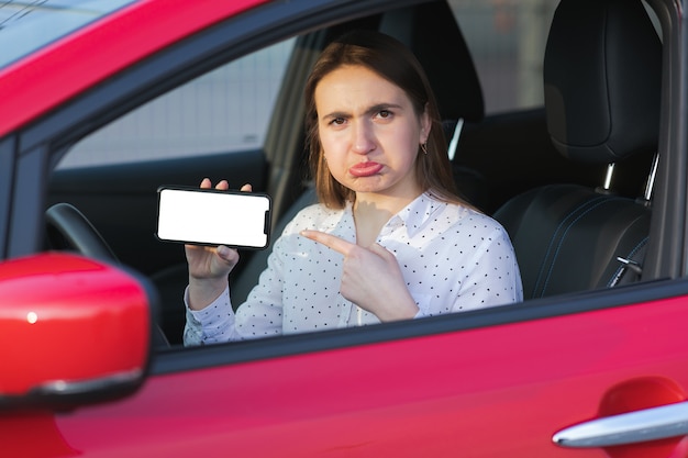 Aplicación móvil para transporte ecológico. Carga de coche eléctrico y mirando la aplicación en el teléfono móvil. Cerca de la pantalla del teléfono inteligente. Mano que sostiene el dispositivo inteligente con pantalla en blanco.