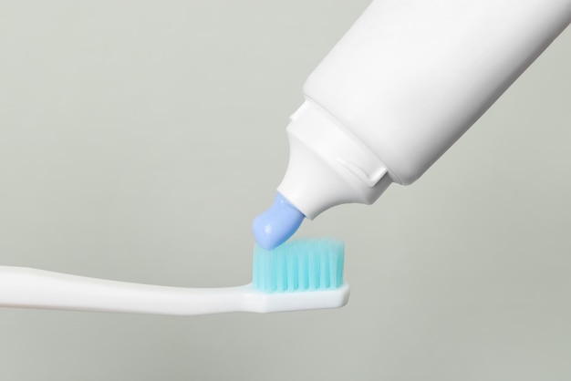 Aplicación de pasta en el cepillo de dientes contra un fondo gris