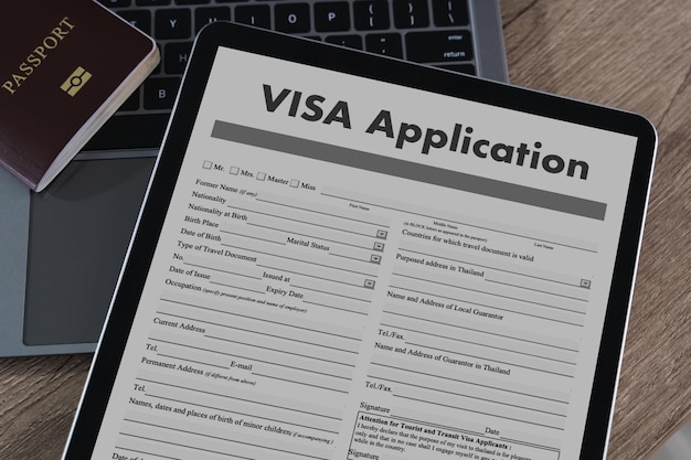 Aplicación de visado tableta digital que muestra el formulario de solicitud de visado con pasaporte y fondo de portátil superficie de madera que representa el viaje