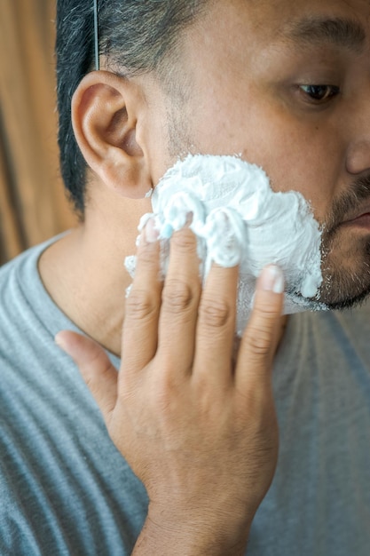 Aplicando creme de barbear no rosto de um homem asiático