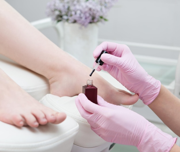 Aplicando esmalte de gel vermelho a um cliente durante uma pedicure