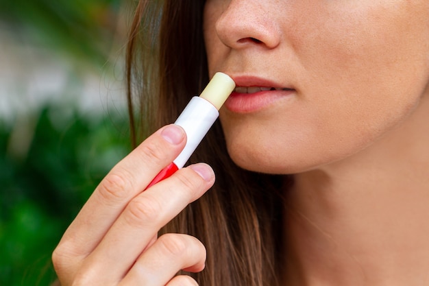 Aplicando lápiz labial higiénico para hidratar los labios secos de cerca al aire libre. cuidado de los labios