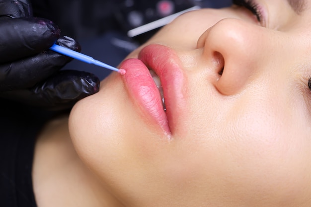 Aplicar anestesia nos lábios da modelo com um pequeno pincel azul antes do procedimento de maquiagem definitiva