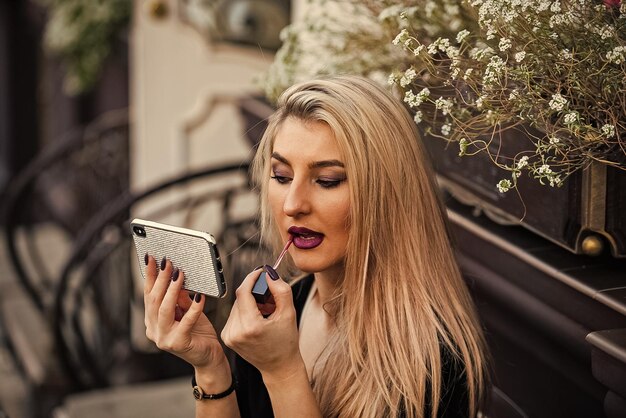 Aplicar maquillaje Chica viendo video tutorial de maquillaje Lápiz labial en labios Cosméticos y maquillaje Prepárate para la cita Siempre luciendo bien Espejo de teléfono inteligente Canal de revisión de cosméticos Concepto de blogger de belleza