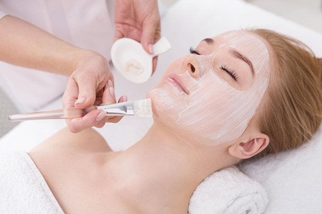 Aplicar mascarilla, tratamiento de belleza spa y cuidado de la piel. Mujer recibiendo mascarilla nutritiva facial por esteticista en el salón de spa, primer plano