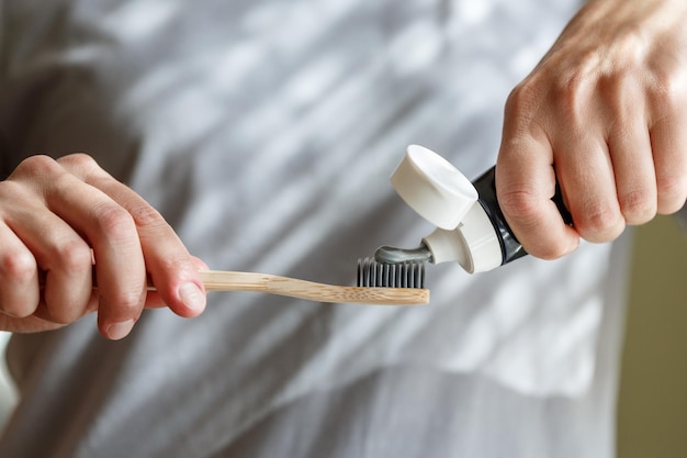 Aplicar pasta de dientes en un cepillo de dientes de bambú Manos apretando el tubo con una pasta de dientes Odontología y concepto higiénico
