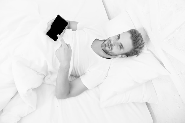 Aplicativo analisa os estágios do sono e te acorda no horário ideal Aplicativos que ajudam a monitorar o sono Homem usa celular na cama Acordar Fornece análise mais profunda do sono Configurar alarme matinal