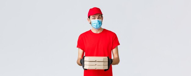 Aplicativo de entrega de alimentos compras online sem contato e conceito covid19 Correio agradável em uniforme vermelho traz pizza em caixas usa máscara facial e luvas de borracha dão ordem de clint