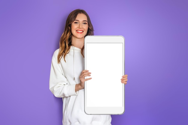 Aplicativo móvel. mulher jovem caucasiana vestindo capuz branco sorrindo e segurando grande smartphone com tela branca em branco, copie o espaço para design. brincar