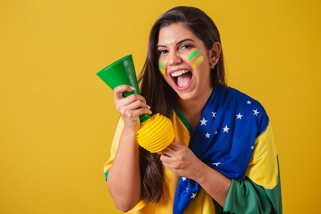 Apoiadora do campeonato de futebol da copa do mundo 2022 do Brasil usando a bandeira do brasil como capa buzinando e festejando no jogo de futebol Horn