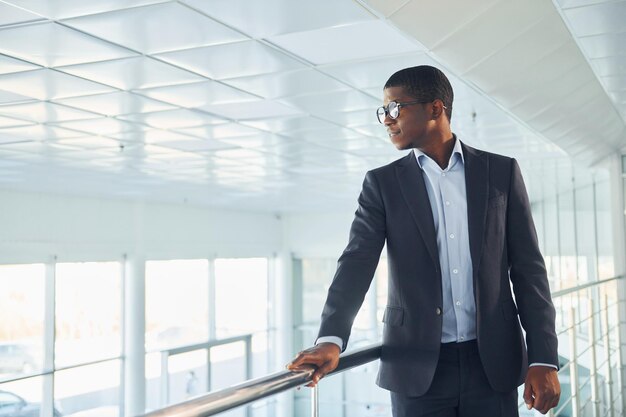 Apoiando-se nos trilhos Jovem empresário afro-americano de terno preto está dentro de casa