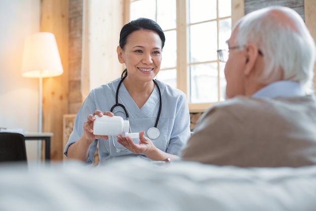 Apoie seu organismo. médico feliz e positivo carregando uma garrafa cheia de comprimidos enquanto olha para o homem mais velho