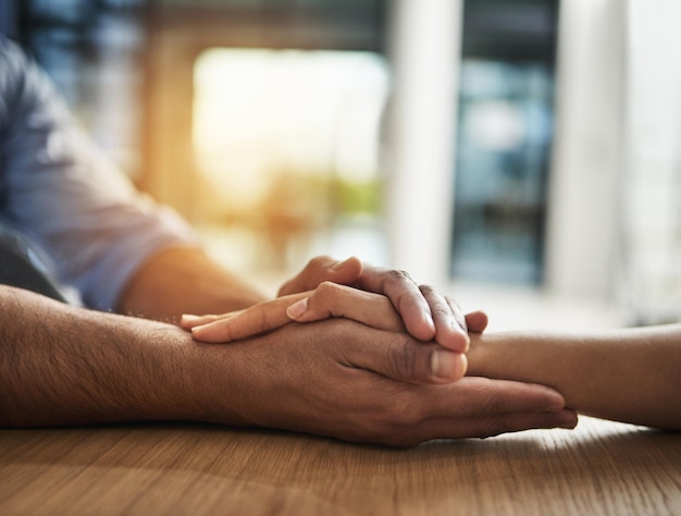 Apoio de bondade e confiança entre duas pessoas de mãos dadas enquanto estão sentados juntos em uma mesa Closeup de duas pessoas conversando em tempos difíceis ou discutindo um problema enquanto demonstram preocupação e amor