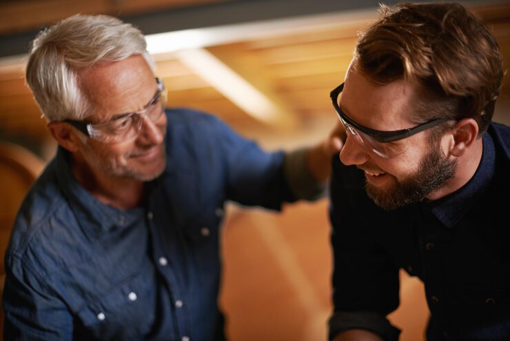 Foto apoio pai e filho em uma oficina arquiteto e família com renovação e óculos de segurança pais homens e trabalho em equipe com trabalho de construção e construção com planejamento para projeto e cooperação