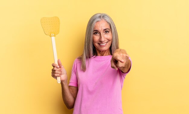 Apontando para a câmera com um sorriso satisfeito, confiante e amigável, escolhendo você e segurando um mata-moscas