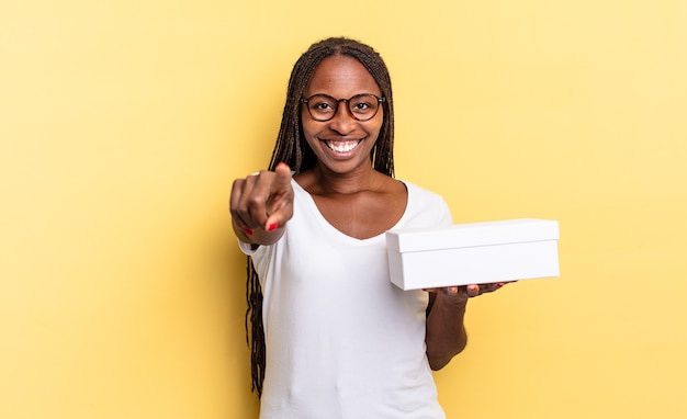 Apontando para a câmera com um sorriso satisfeito, confiante e amigável, escolhendo você e segurando uma caixa vazia