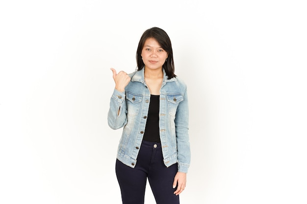 Apontando para o lado esquerdo com o polegar de uma linda mulher asiática vestindo jaqueta jeans e camisa preta
