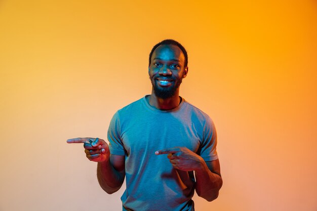 Apontando para o lado. Retrato moderno de homem afro-americano na parede laranja do estúdio